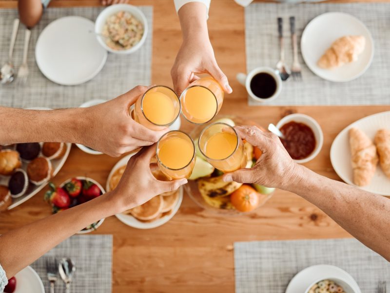 Lunch, hands and people toast with orange juice, beverage or glass drinks at lunch, brunch or food